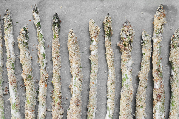 coated asparagus lined up on parchment paper