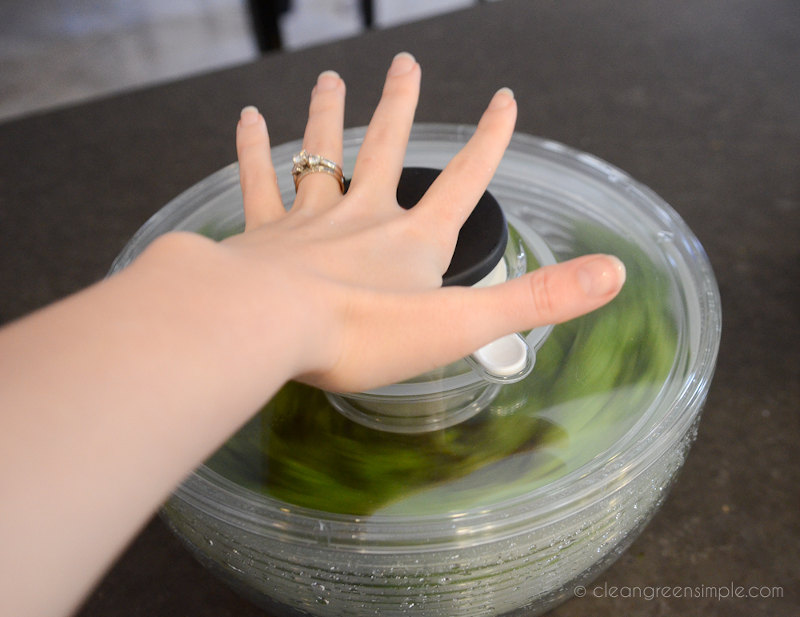 Woman's hand pressing down on salad spinner