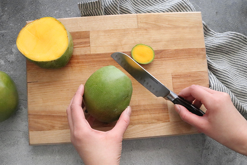 cutting the ends off of a mango on a cutting board