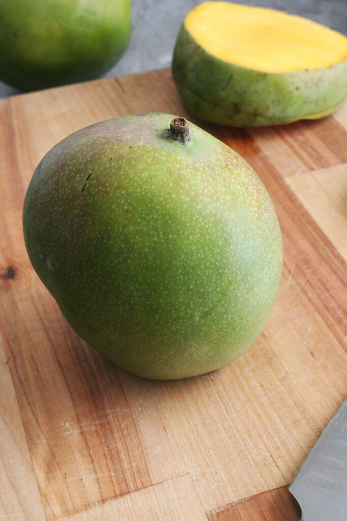 a whole mango on a cutting board