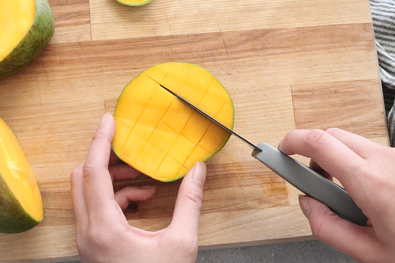 scoring across the flesh of a mango in the opposite direction with a paring knife