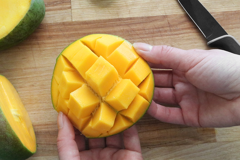 Pushing the peel of a mango upward until the cubes of mango pop out