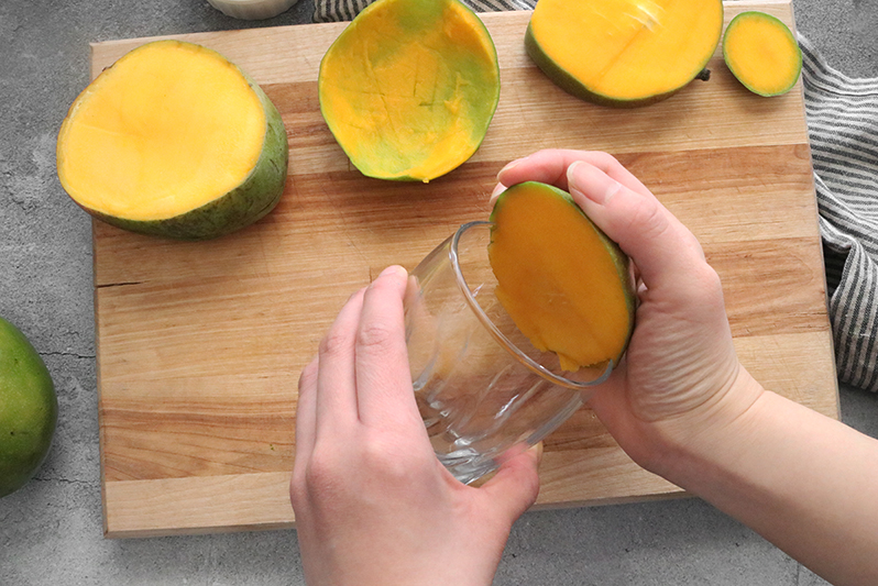 scooping out mango flesh with a glass