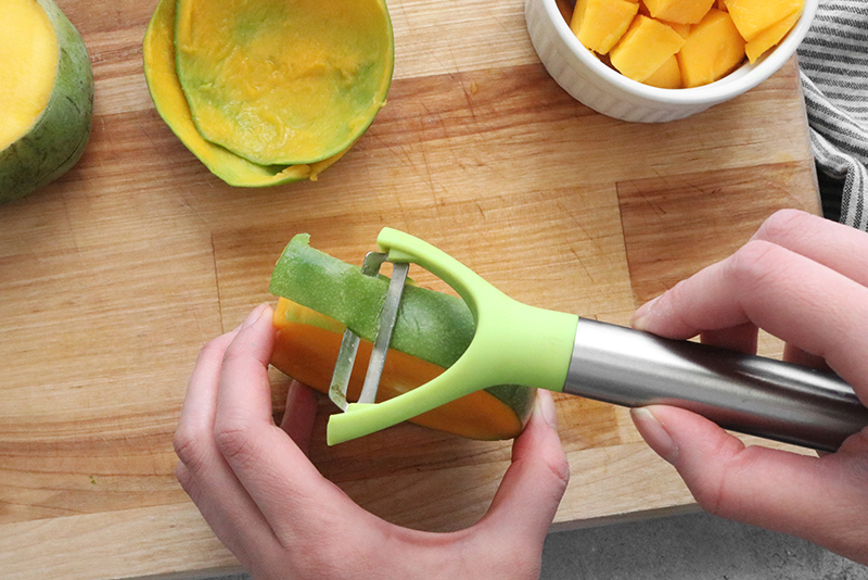 using a peeler to cut off skin of a mango