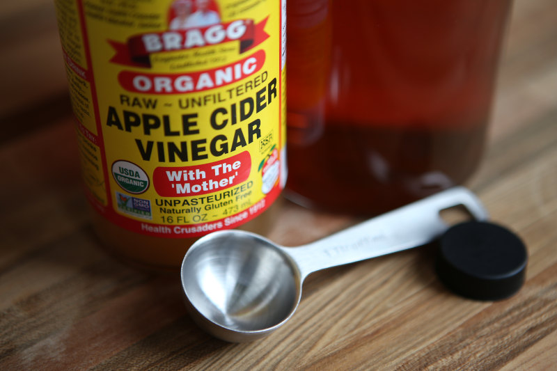 Bragg Apple Cider Vinegar on wooden table with a measuring spoon