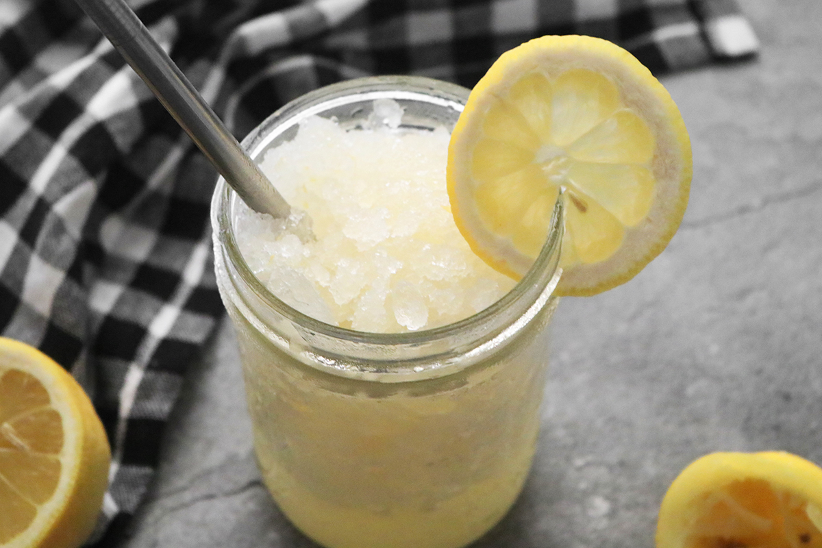 Frozen lemonade in a ball jar glass with lemon garnish and a metal straw