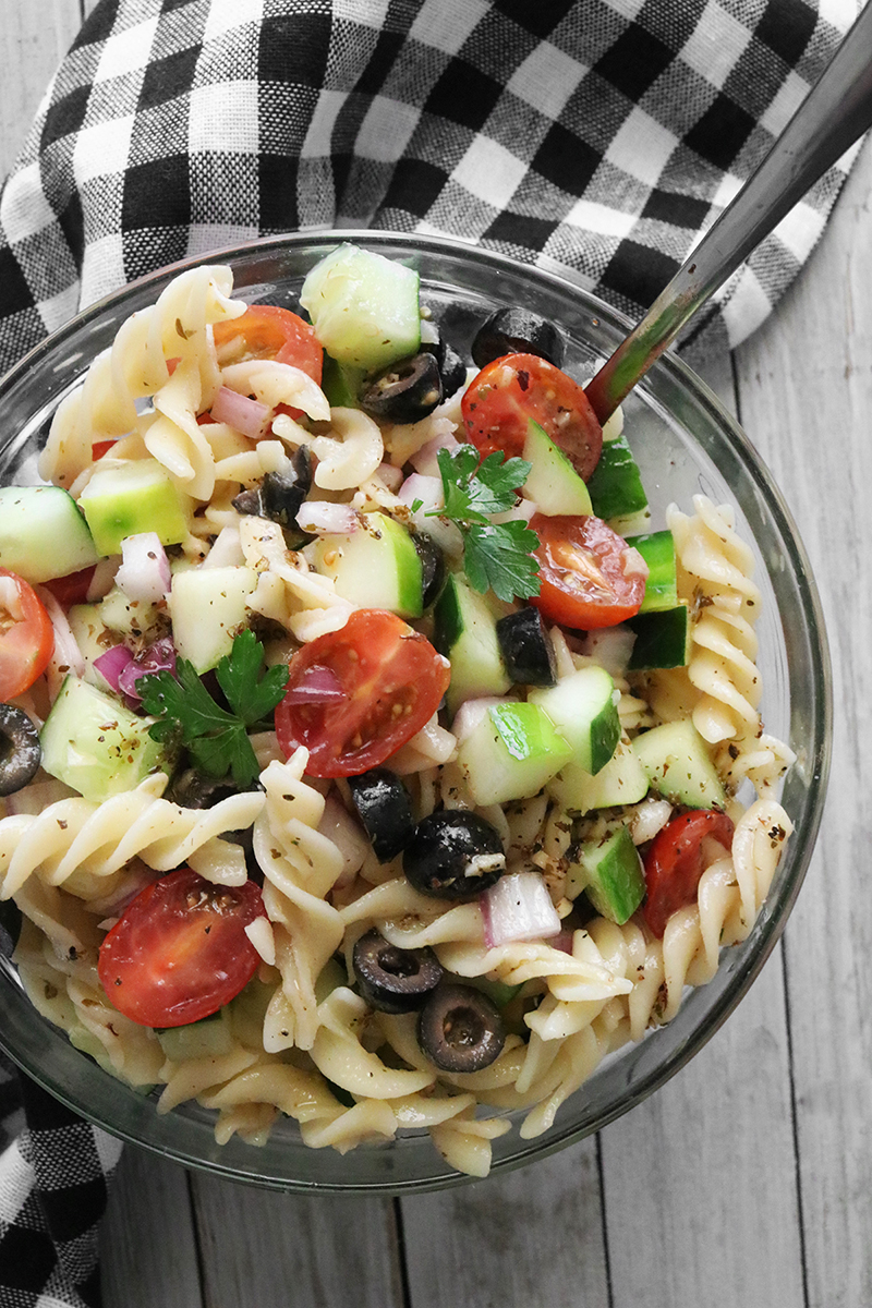 Pasta salad with tomatoes, cucumbers, and olives in a glass bowl.