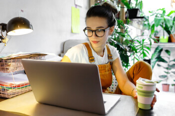 Young female in glasses sitting at computer with house plants in background