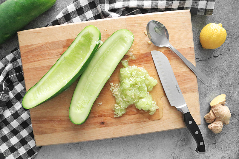 Cucumbers with seeds scooped out with a spoon on a cutting board.