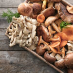 Wicker tray with different types of raw mushrooms on wooden table