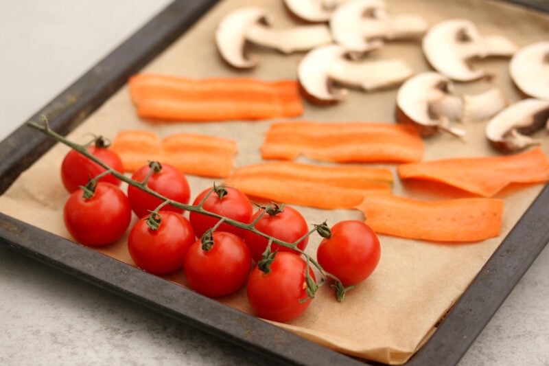 Tomatoes, thinly sliced carrots, and mushrooms arranged on a baking sheet with parchment paper.