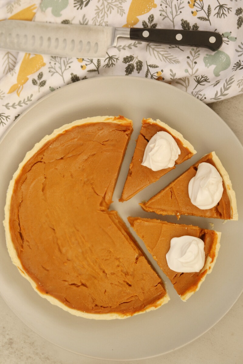 Vegan sweet potato pie cut into slices and served with whipped coconut cream.