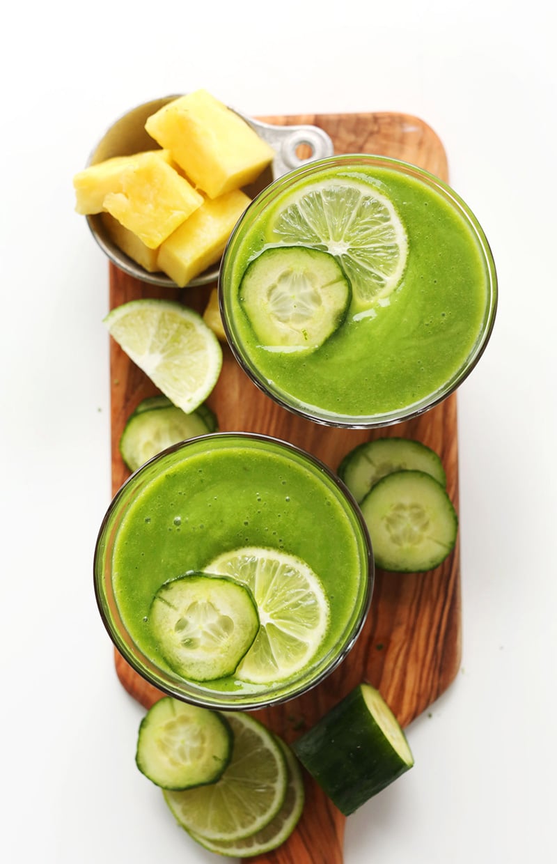 Two glasses of green smoothie dressed with sliced cucumber and lime.