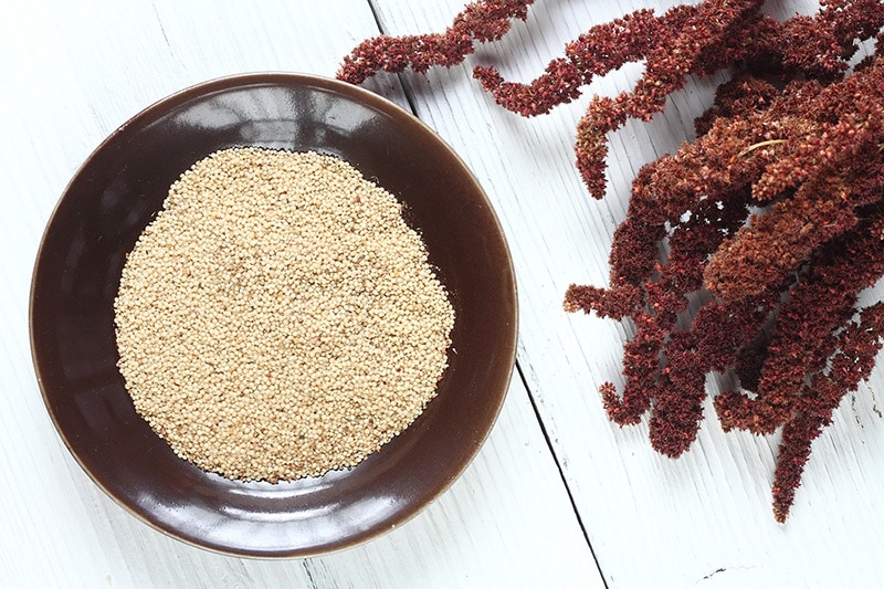 A bowl of amaranth seeds, sitting on a table next to amaranth flowers.