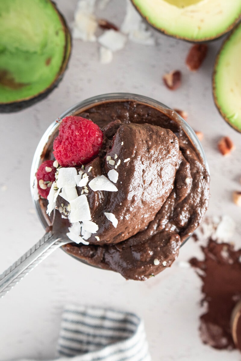 Vegan avocado chocolate pudding in a glass, topped with shaved coconut and raspberries.