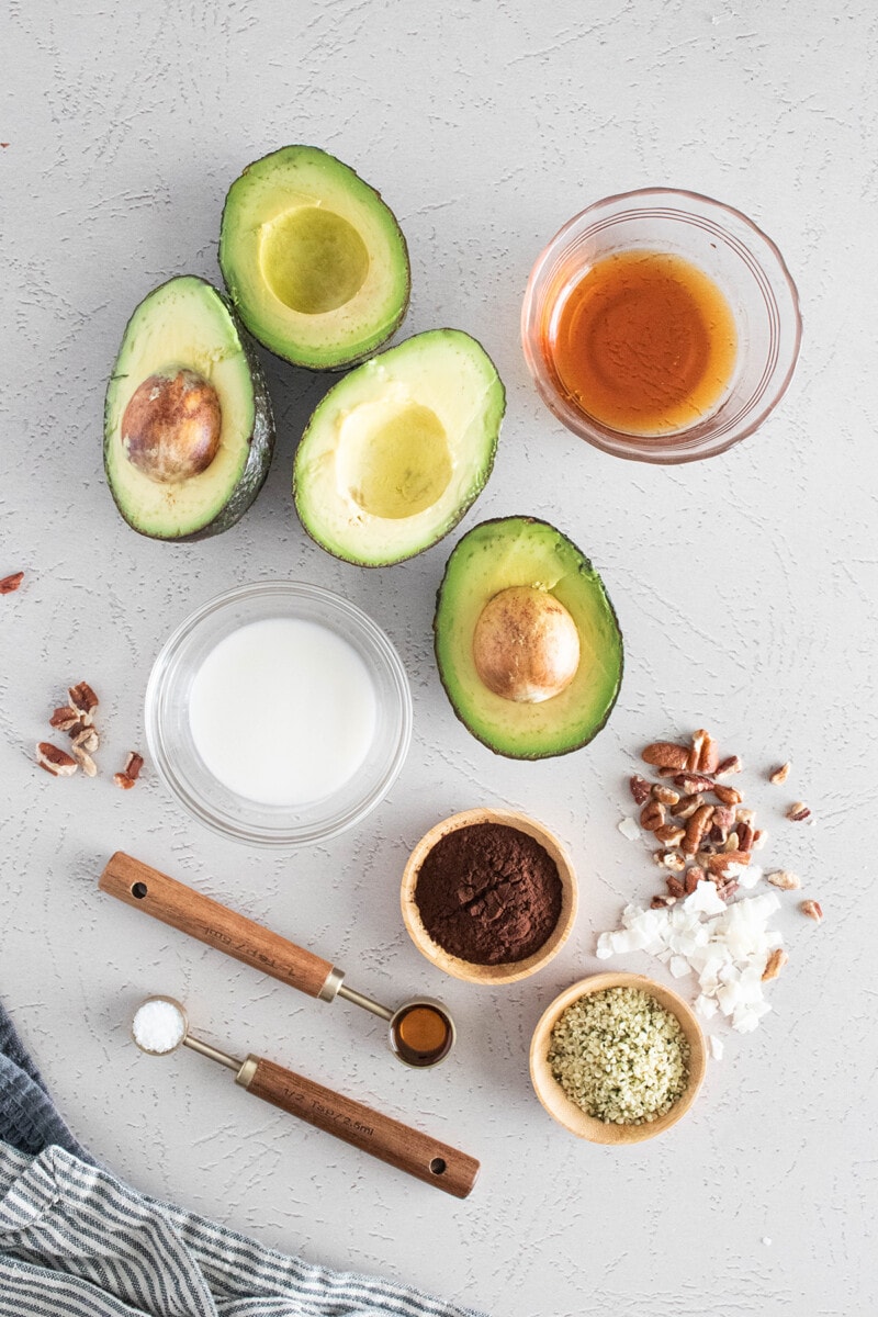 Ingredients for avocado chocolate pudding: Ripe avocado, maple syrup, plant-based milk, and coco powder.