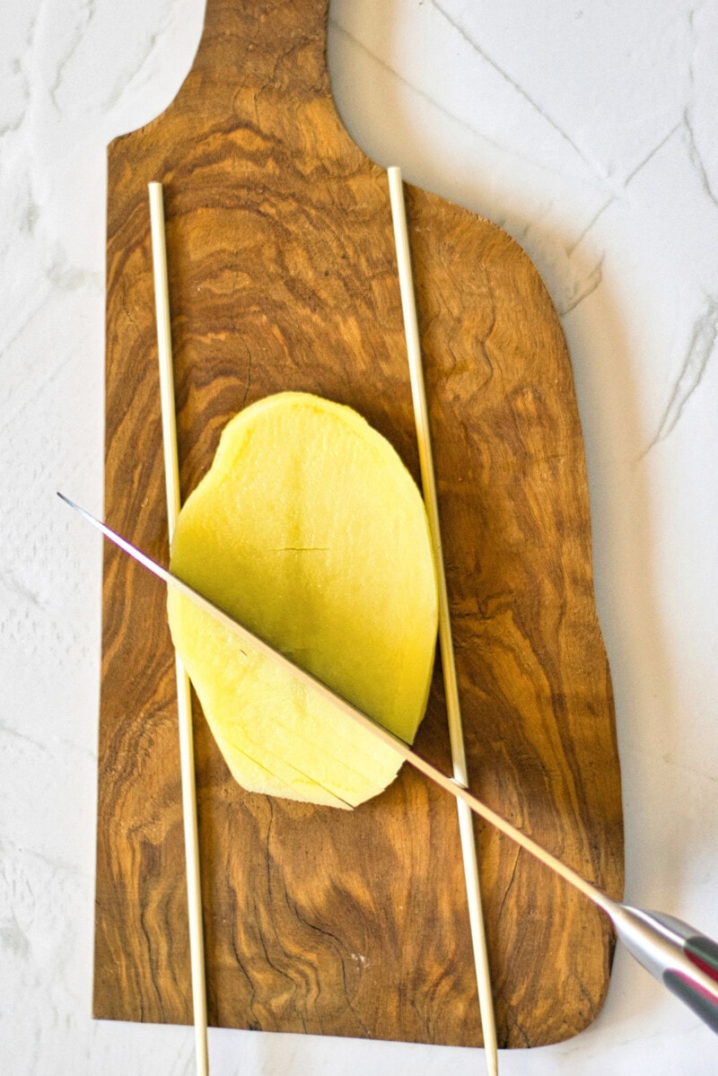 A 1/2" potato slab on a cutting board, cutting shallow, diagonal grooves.