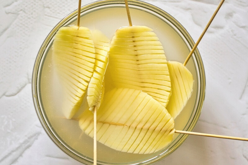 Skewered accordion potato slices in a bowl of water.