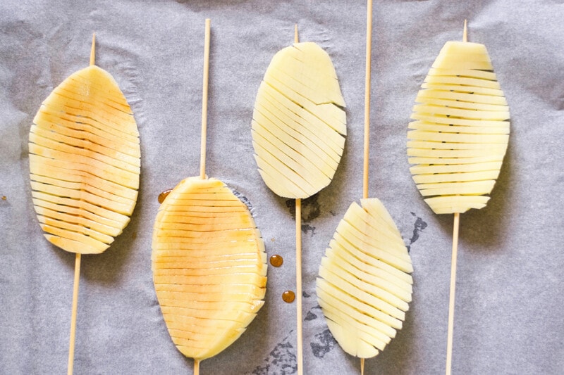 Skewered accordion potato slices on a baking tray lined with parchment paper, brushed with olive oil and paprika.