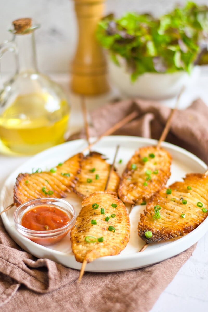 Baked accordion potatoes, topped with sliced green onions, on a plate.