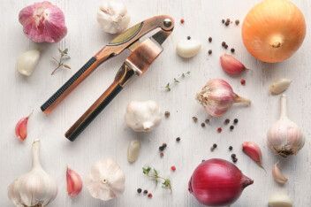 A metal garlic press sitting next to several whole cloves of garlic on a clean surface.