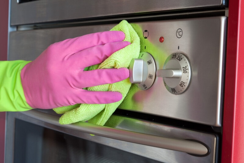 Hand wearing a rubber glove and using a microfiber cloth to clean the surface of an oven.
