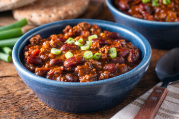 Classic vegan chili in a blue bowl with chopped spring onions on a wooden table
