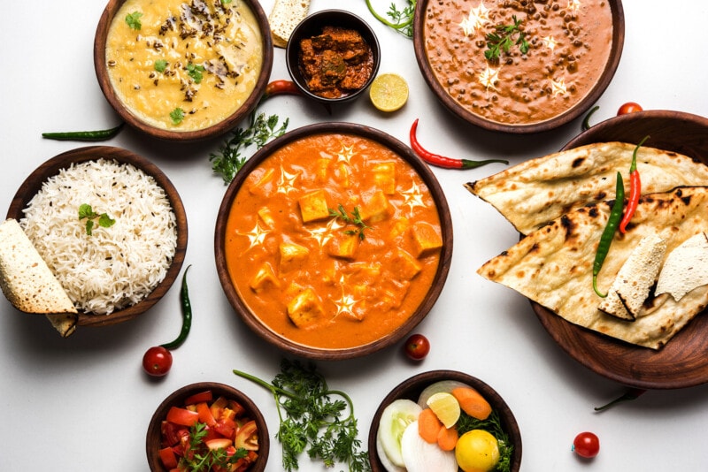 Assorted Indian food, including rice, lentils, paneer, dal makhani, naan, chutney, and spices.