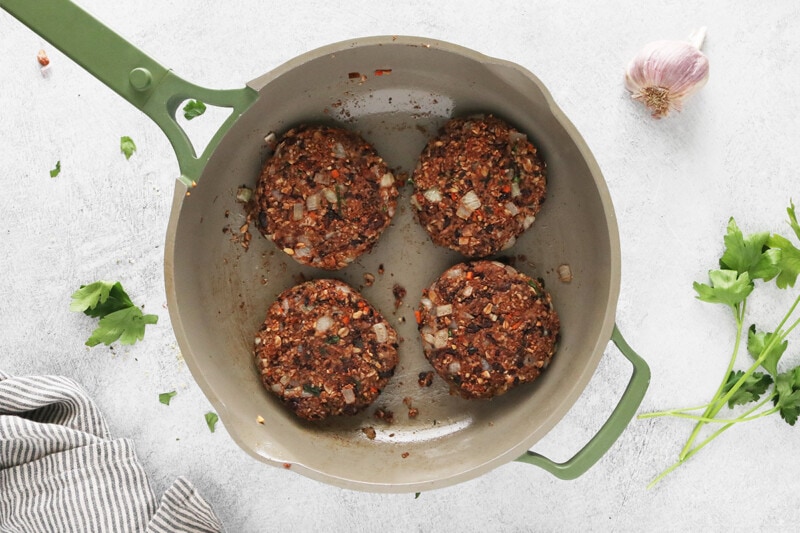 Formed black bean burger patties cooking in a large skillet.