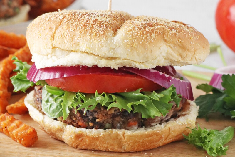 Vegan black bean burgers with oats, served on a bun with tomato, lettuce, and red onion.