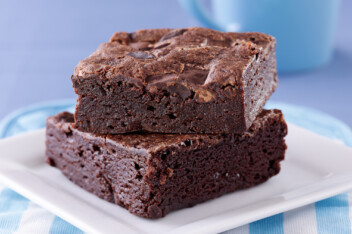 Two brownies stacked on a while plate with a blue background