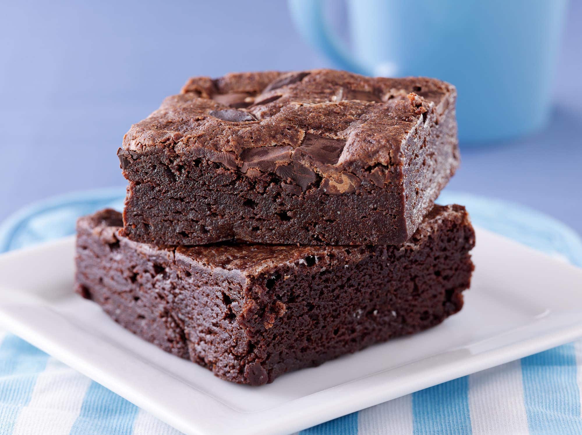 Two brownies stacked on a while plate with a blue background