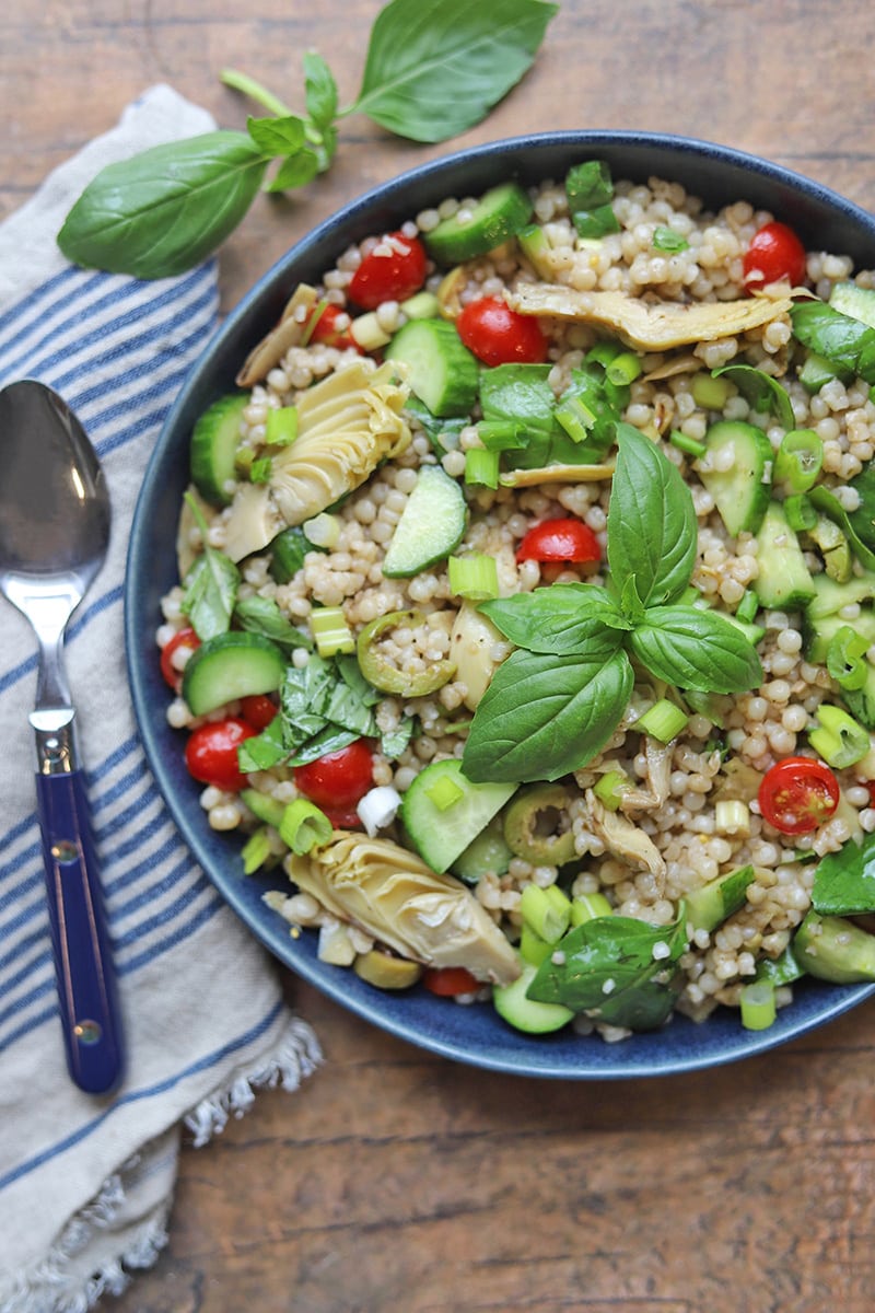 Israeli couscous salad with artichokes, cucumber, and tomato in a bowl.