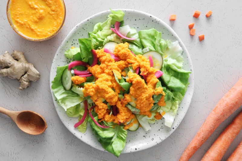 Fresh green salad on a plate, topped with carrot ginger dressing.