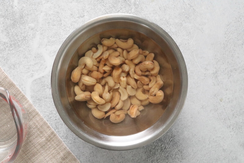 Cashews and hot water in a stainless steel bowl.