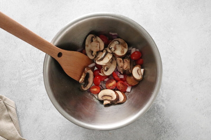 Mushrooms, onions, and cherry tomatoes in a stainless steel bowl.