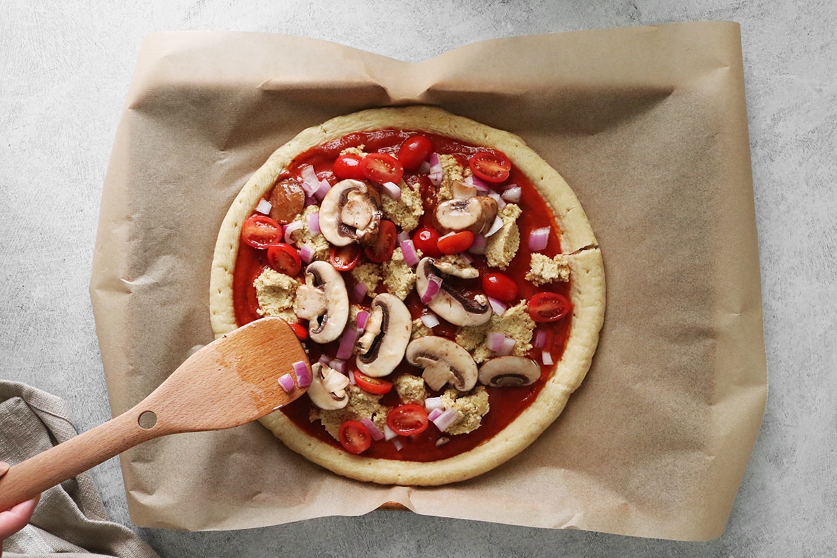 Adding vegetables to a cashew ricotta pizza.