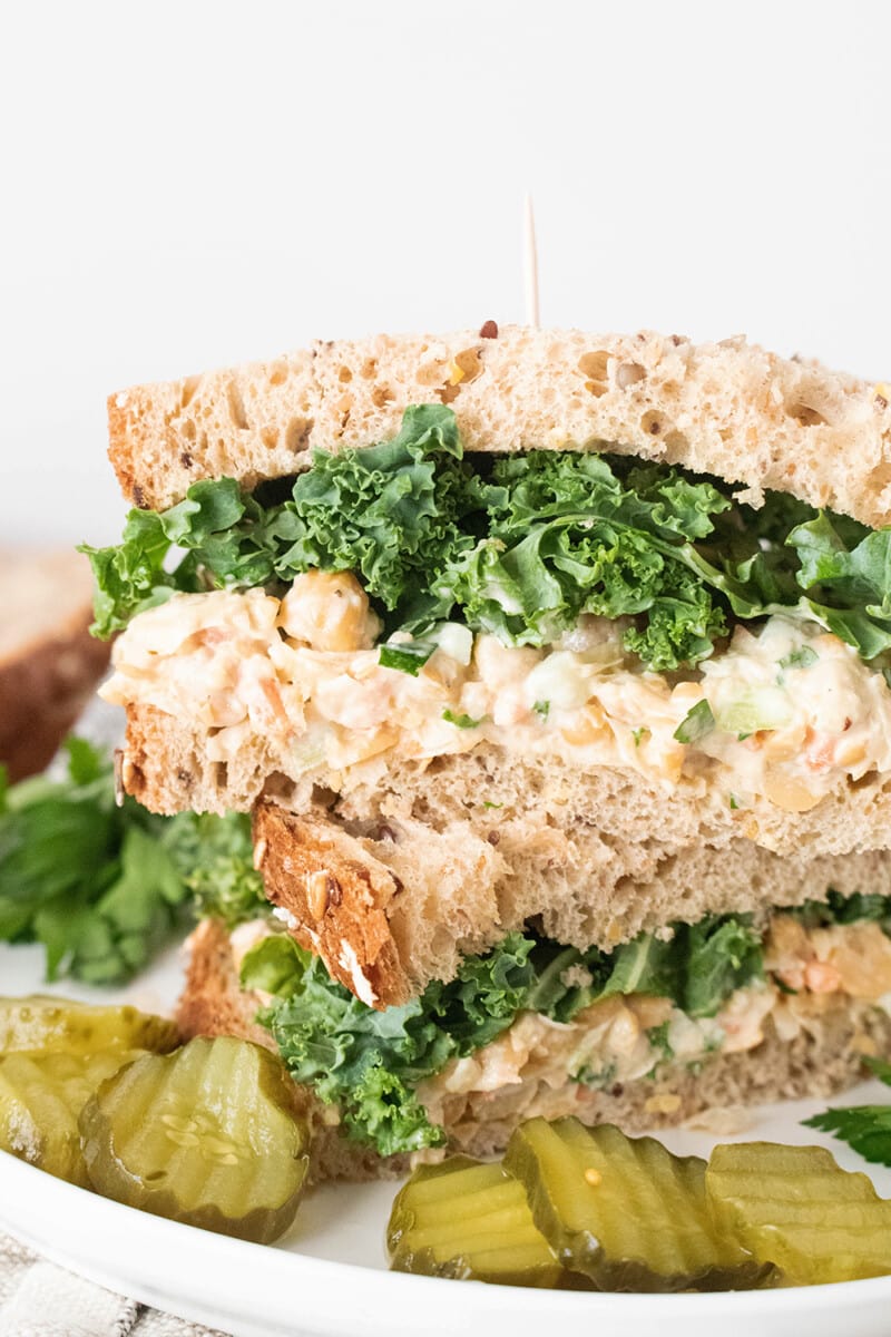 Chickpea salad sandwich with kale and pickles on a plate.