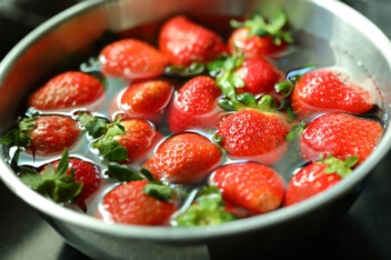 Cleaning strawberries in vinegar and water in a stainless bowl.