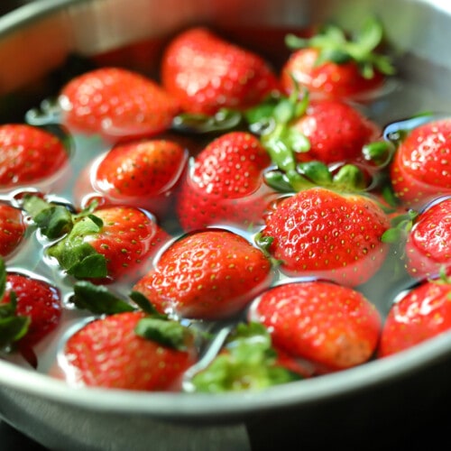 Cleaning strawberries in vinegar and water in a stainless bowl.