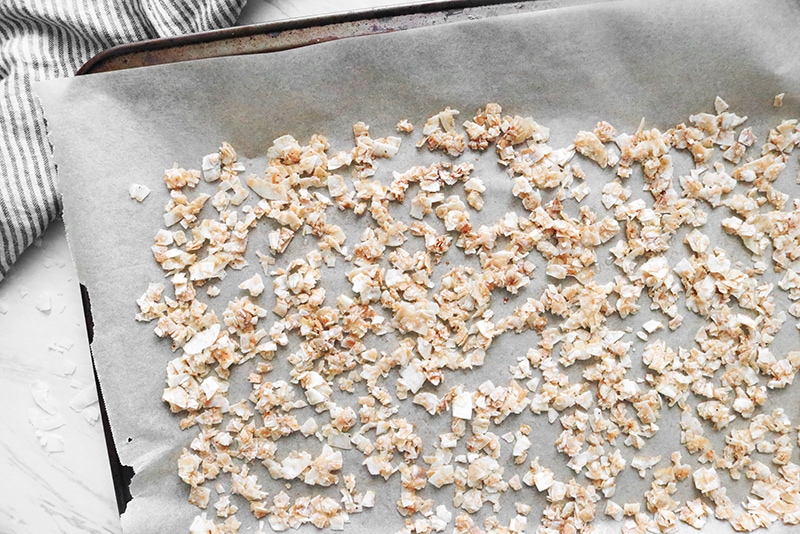 Seasoned coconut flakes spread on a parchment lined baking sheet