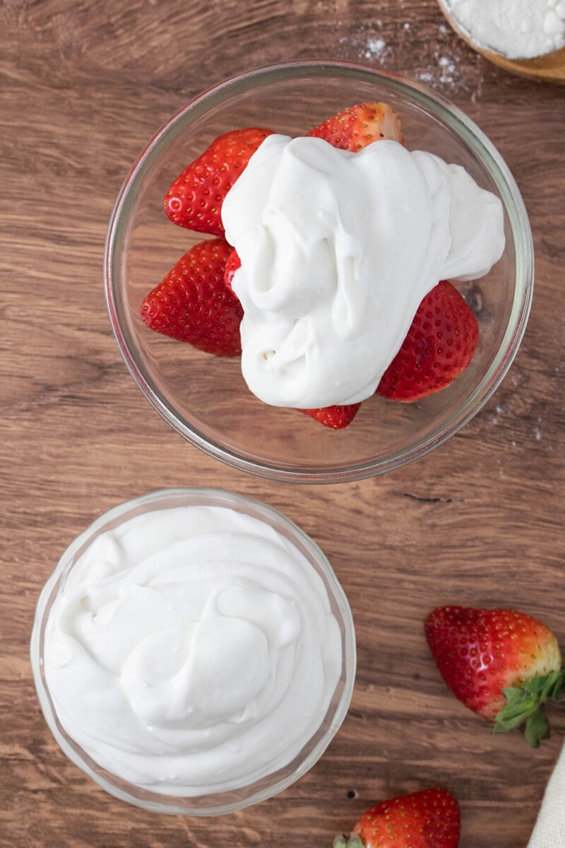 A bowl of fresh strawberries topped with a large dollop of coconut milk whipped cream.