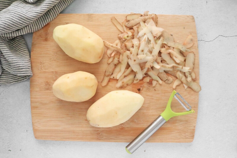 peeled potatoes on a cutting board with a potato peeler