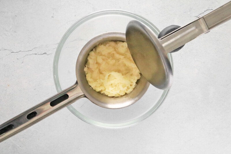 potato ricer filled with grated potatoes over a glass bowl