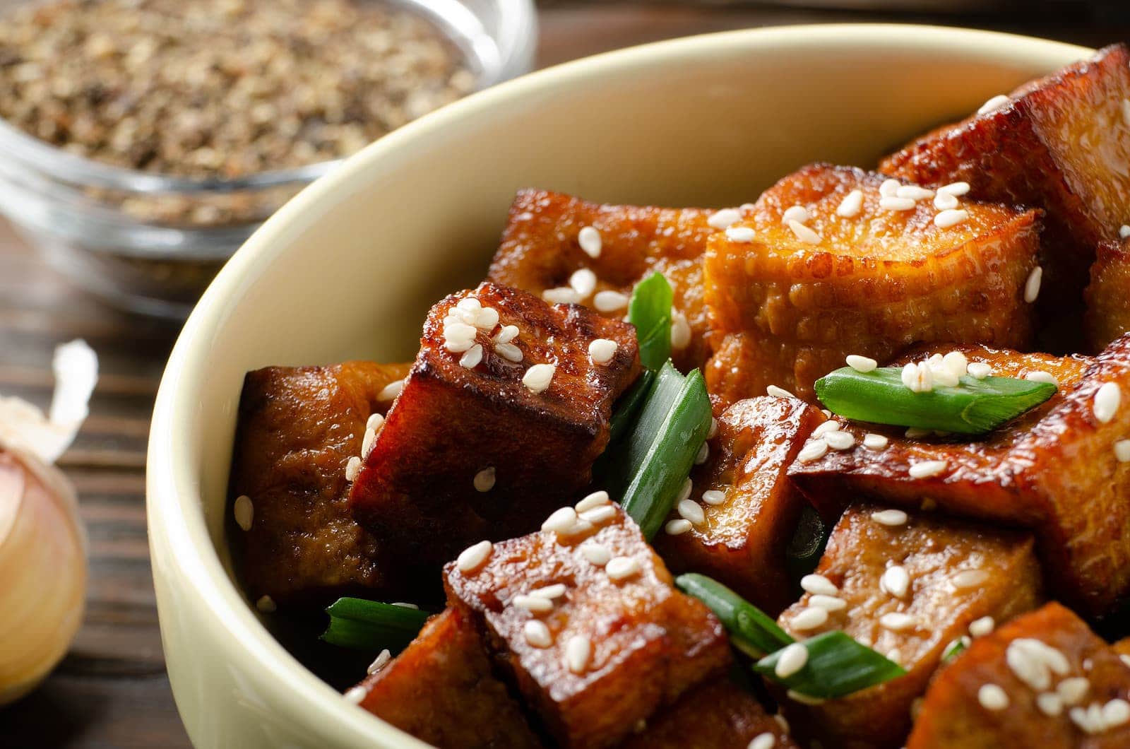 Close Up view at crispy fried tofu pieces with chives and sesame in clay dish