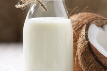 Coconut Milk in a glass bottle with coconuts on a table