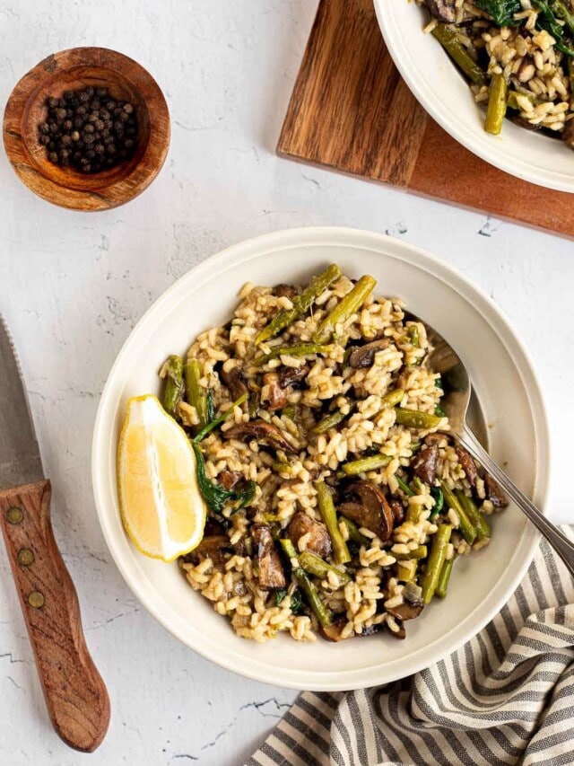 Top view of Mushroom and Asparagus Risotto in a white bowl with a lemon slice.