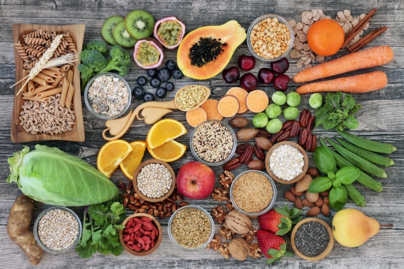 A wooden table filled with fresh, whole foods, including fruits, vegetables, and whole grains