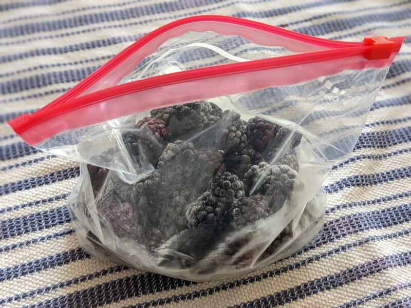 Frozen blackberries in a ziploc bag on a dish towel.