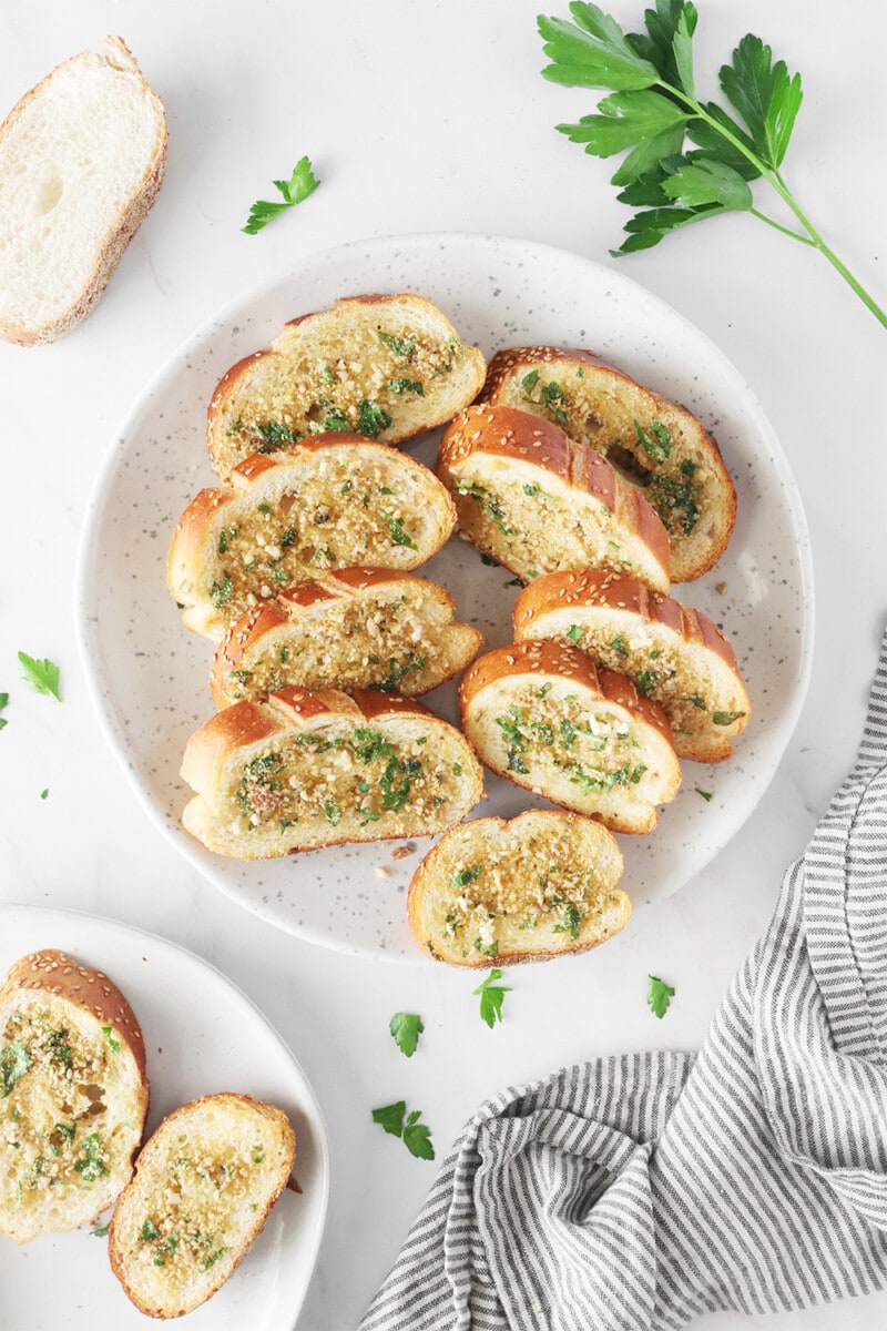 Vegan garlic bread, sprinkled with vegan Parmesan and fresh parsley on a white plate.